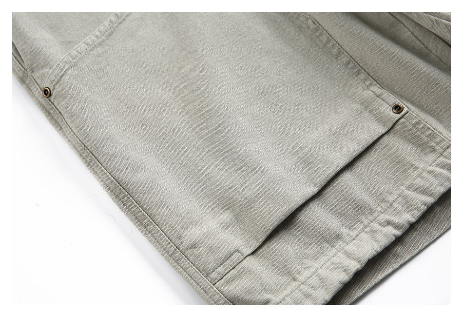 Close-up of a large stitched pocket and hem on light gray-beige bottoms, with metal rivets at the corners.