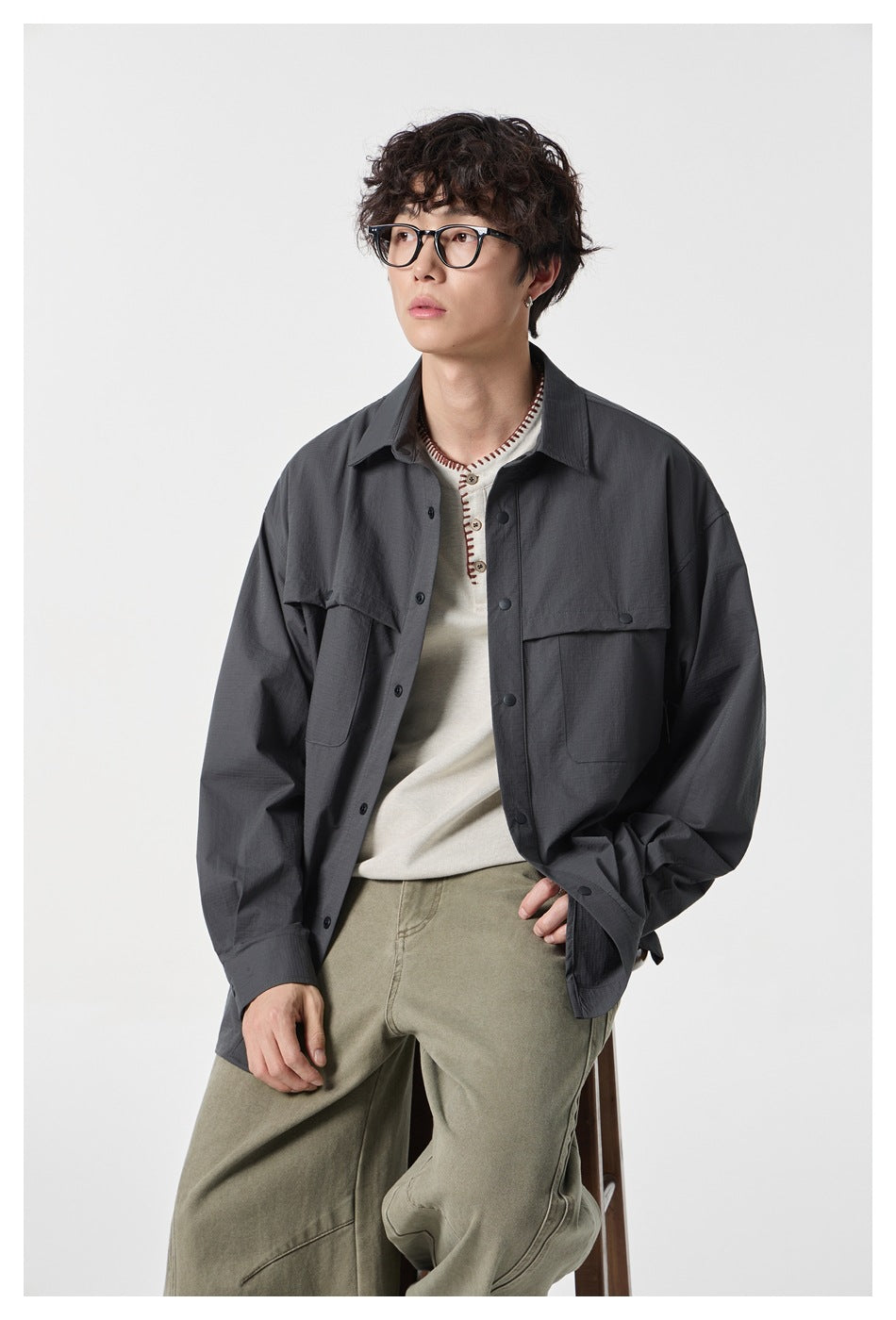 Model wearing an open charcoal oversized button-up shirt with flap chest pockets, shown from the front.
