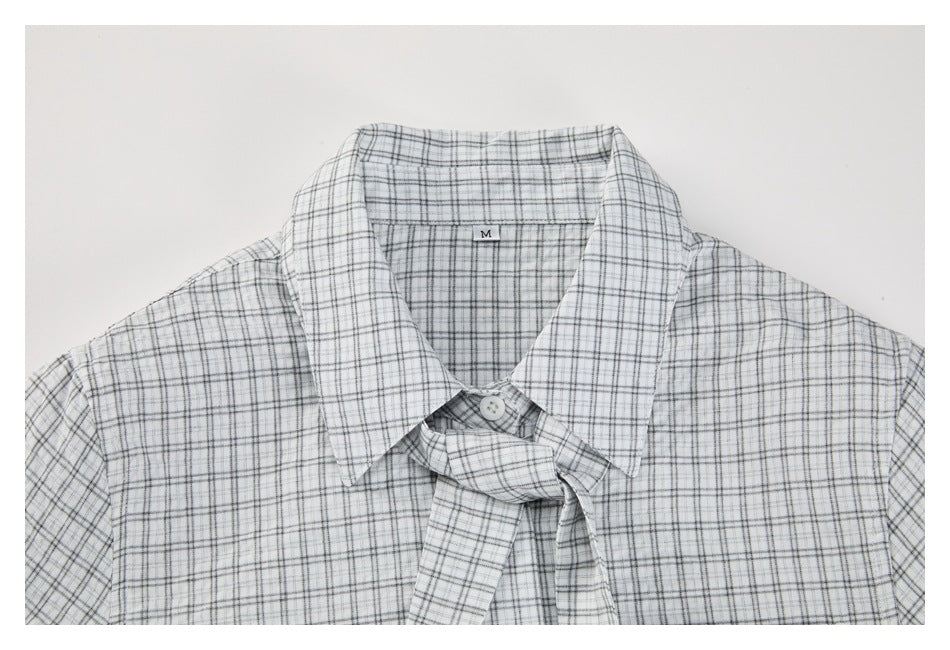 Upper front of a white shirt with a gray and black plaid pattern, pointed collar, and matching necktie detail.