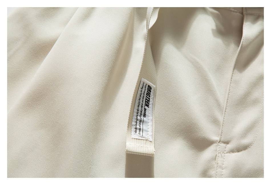 Close-up of a branded fabric tag on the beige shorts' webbing belt beside the garment seam.