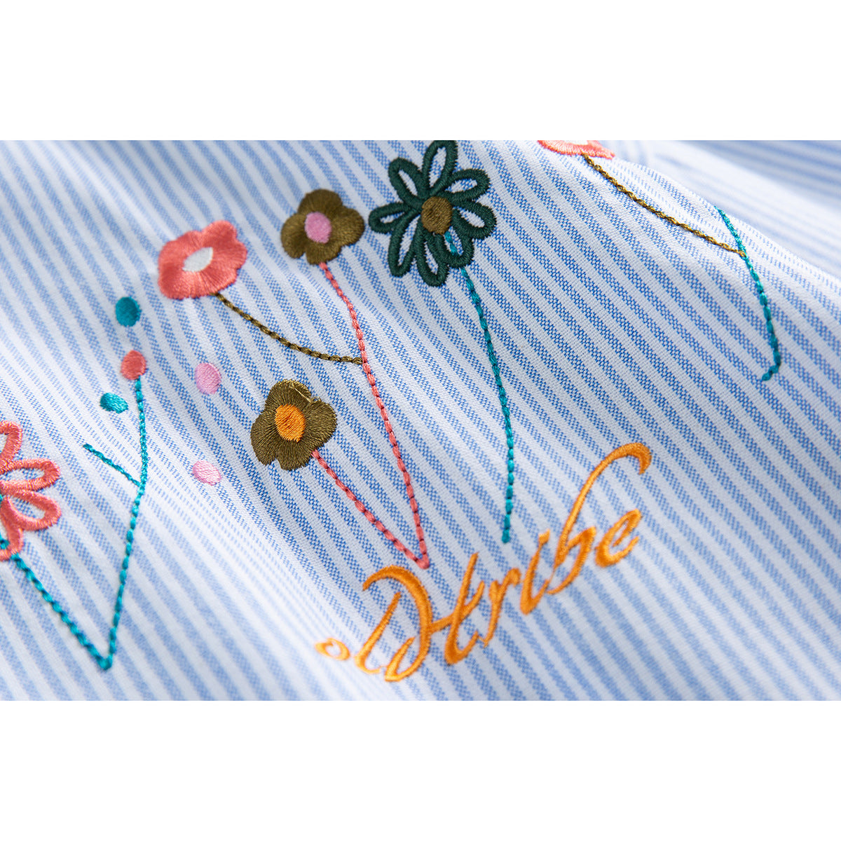 Close-up of colorful embroidered flowers and orange script on blue-and-white pinstriped fabric.