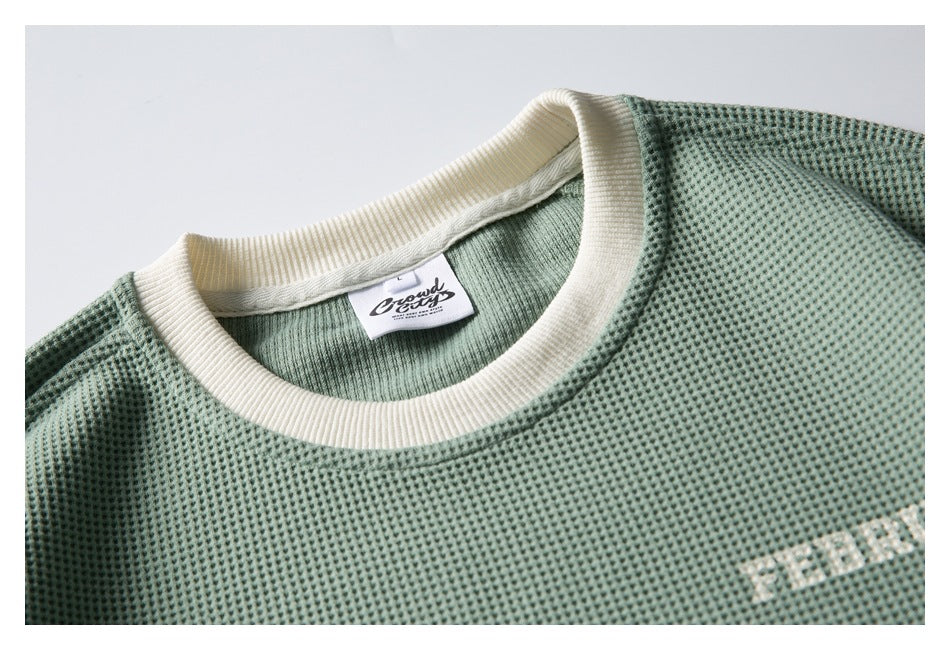 Close-up of a sage-green textured shirt with an ivory ribbed crew neck and a sewn-in label.