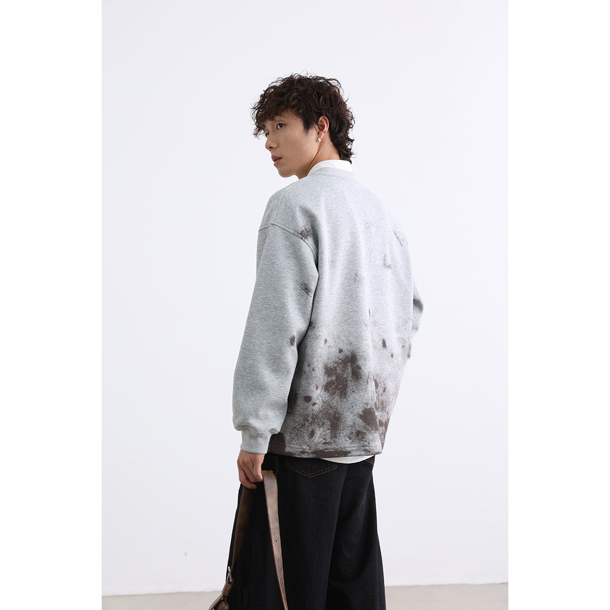 Model turned to show the back of a light gray oversized sweatshirt with dark distressed marks.