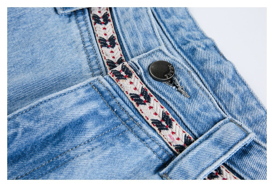 Close-up of light-wash jeans with a black button, belt loop and cream patterned waistband trim.
