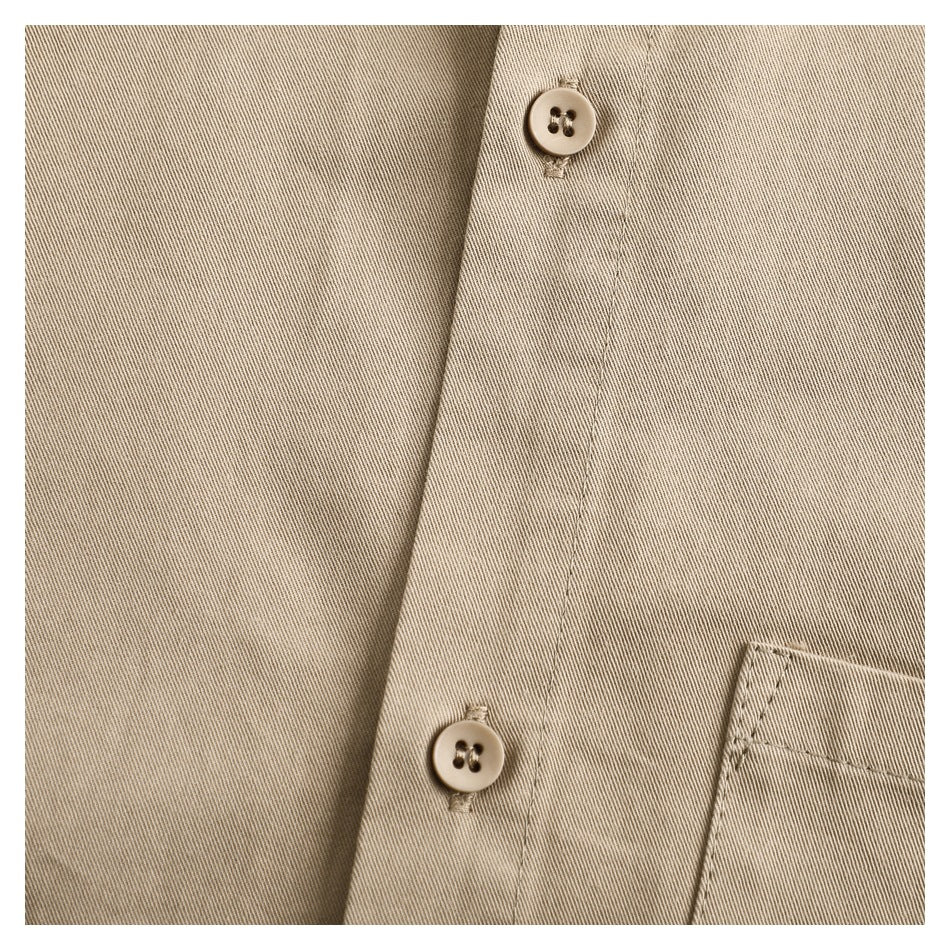 Close-up of two tan shirt buttons and part of a chest pocket on beige fabric.