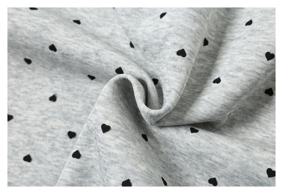 Close-up of light gray heathered fabric with scattered black hearts, gathered to show its folds.