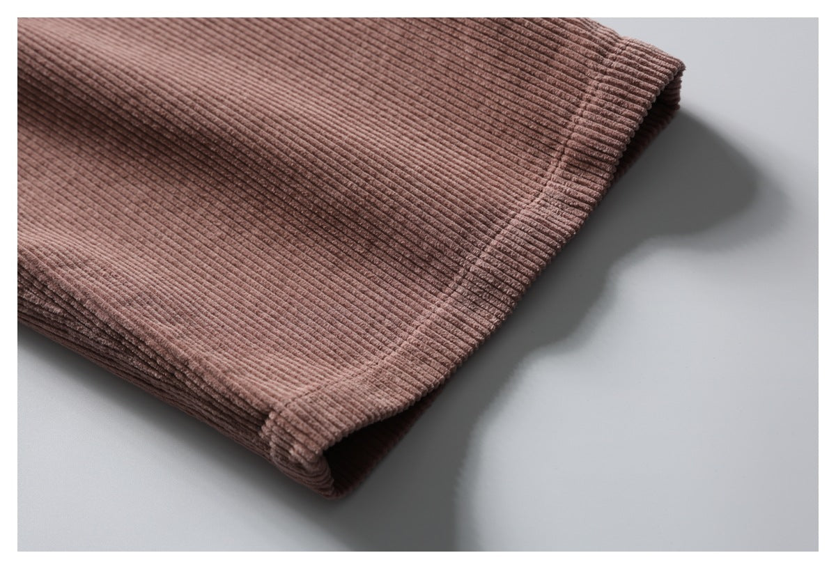 Close-up of a dusty mauve-brown ribbed trouser hem folded over a pale surface.