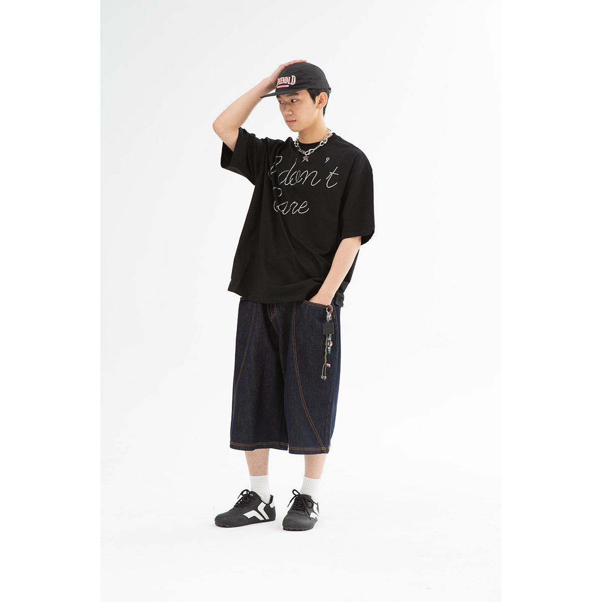 Model wearing an oversized black T-shirt with white cursive lettering and dark denim shorts.