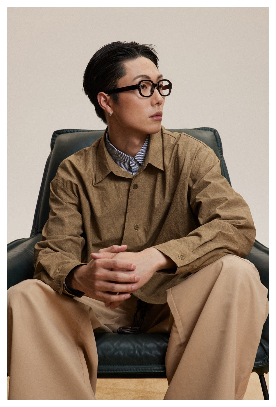 Close view of a seated model wearing a brown button-up shirt with a pointed collar and button cuffs.