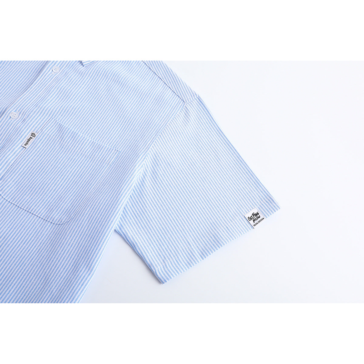Close-up of a light blue and white striped shirt pocket and short sleeve, with small sewn-in labels.