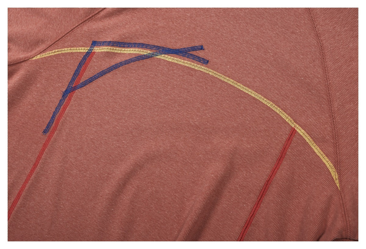 Close-up of multicolored curved and angular stitching on dusty rose ribbed fabric.