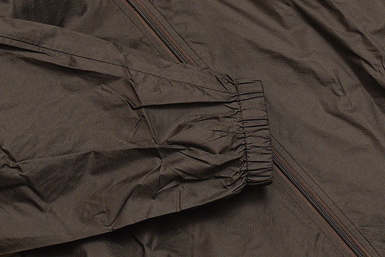Close-up of a dark jacket sleeve and gathered elastic cuff beside the front zipper.