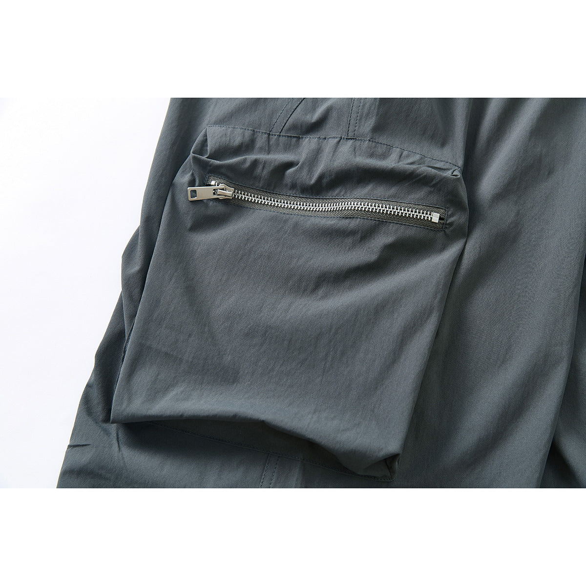 Close-up of a dark charcoal pants cargo pocket with a horizontal silver zipper.