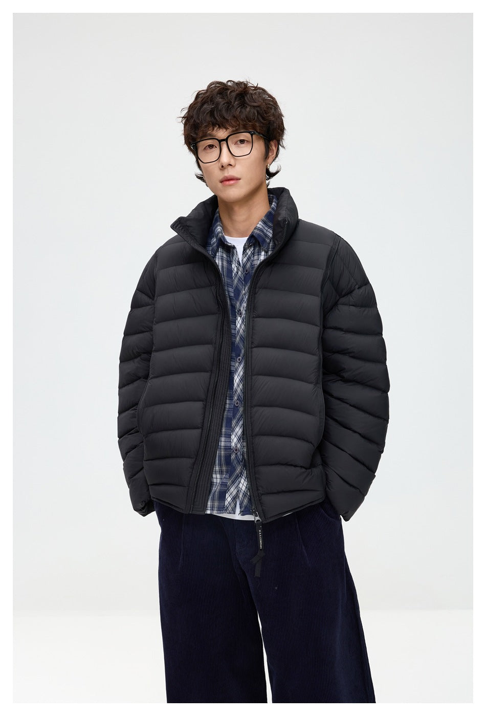 Closer view of a model wearing a black horizontally quilted puffer jacket open over a blue plaid shirt.