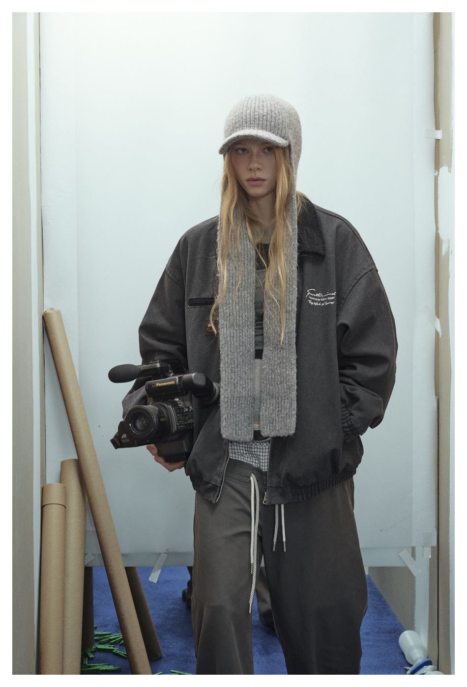 Front view of a model in an oversized charcoal zip jacket and wide-leg pants, with a gray cap and scarf.