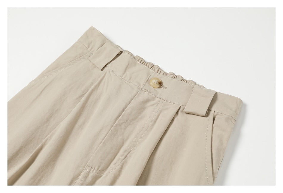 Close-up of cream trousers showing the front waistband, button, belt loops and pleats.