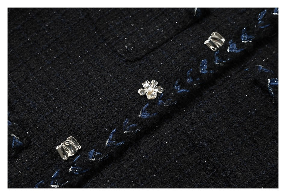 Close-up of black textured jacket fabric with blue embroidered edging and ornate silver-tone fasteners.