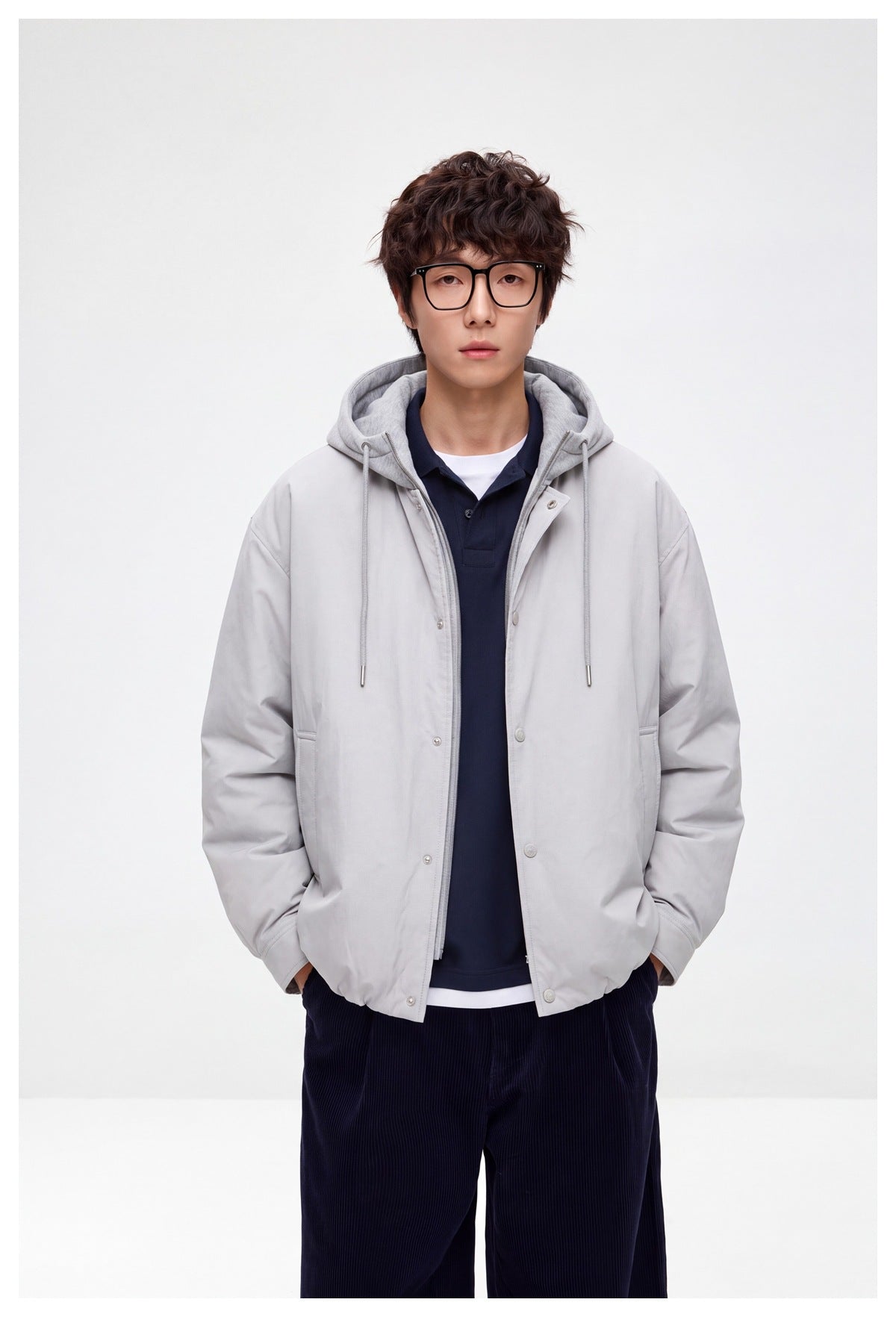 Front view of a model wearing a light gray hooded snap-front jacket with drawstrings and front pockets.
