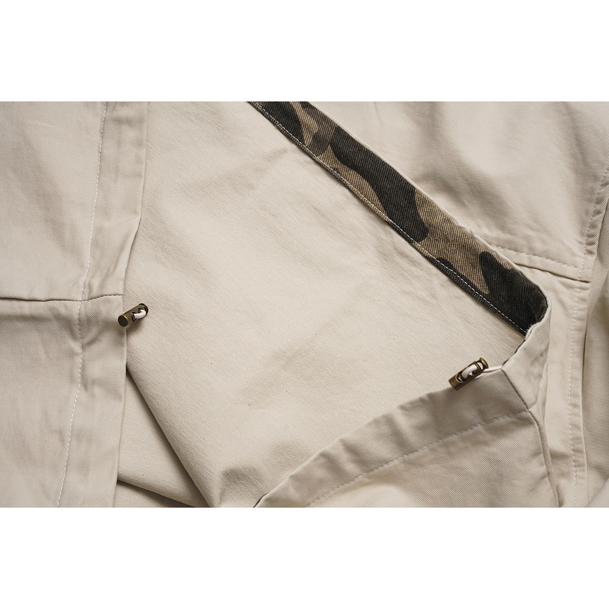 Close-up inside a beige shirt showing camouflage lining and two small metal fasteners.