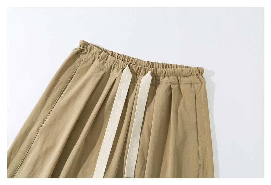 Close-up of tan pants showing the elastic waistband, front pleats, and white drawstrings.