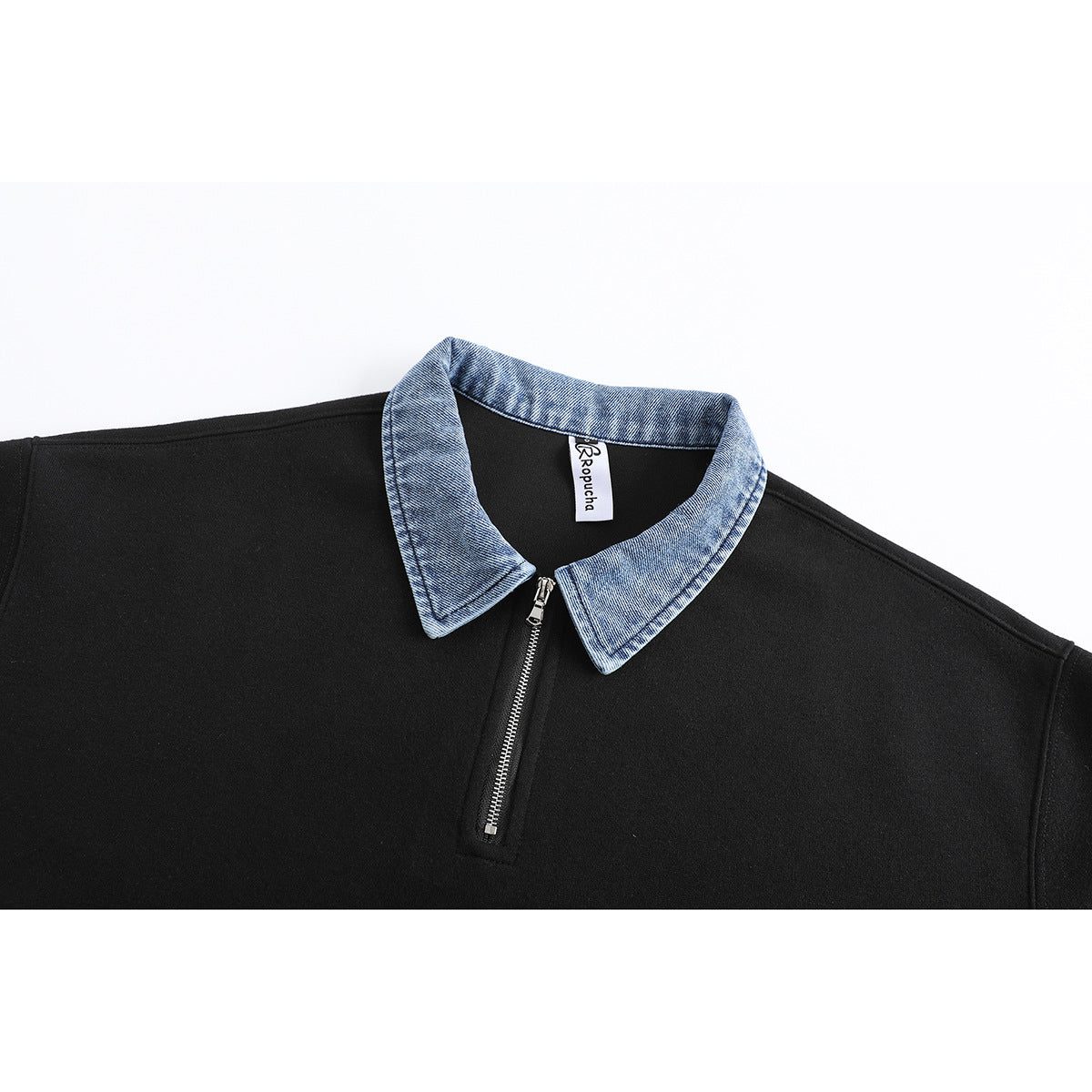 Close-up of a black pullover with a blue denim pointed collar and silver half zipper.