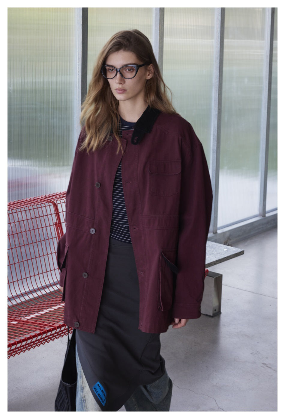 Model wearing an oversized burgundy button-front jacket with black collar and multiple pockets.