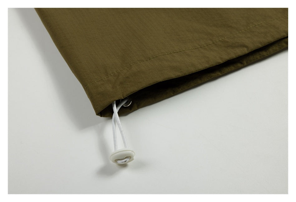 Close-up of an olive-brown garment hem with a white drawcord and toggle.