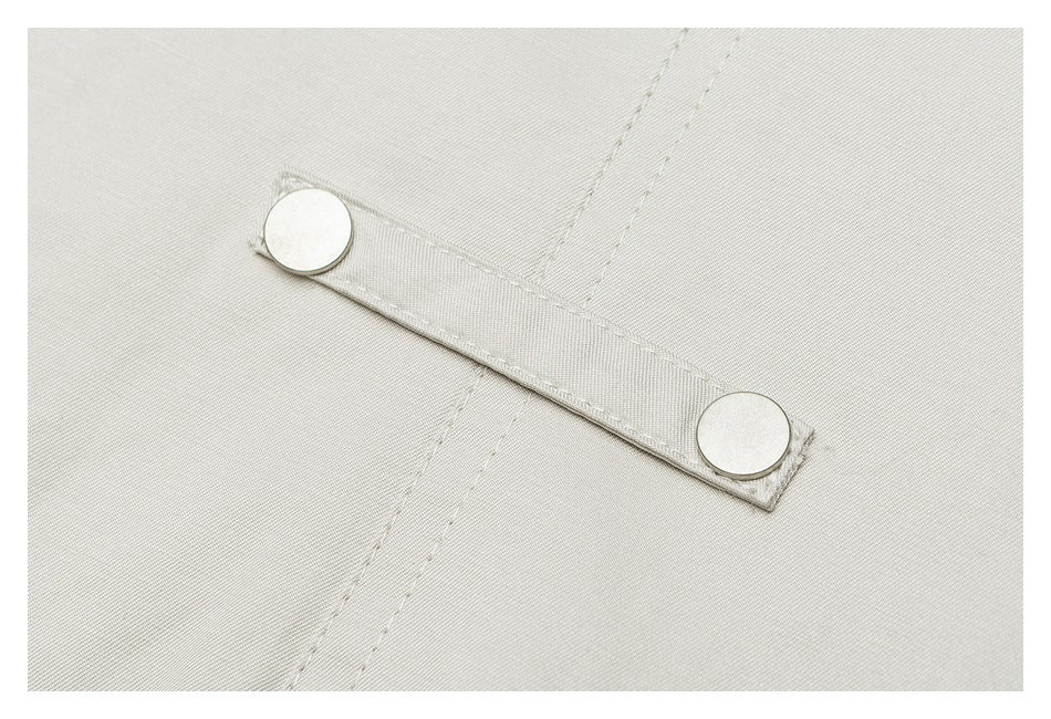 Close-up of a light beige jacket panel with a narrow tab secured by two silver snaps.