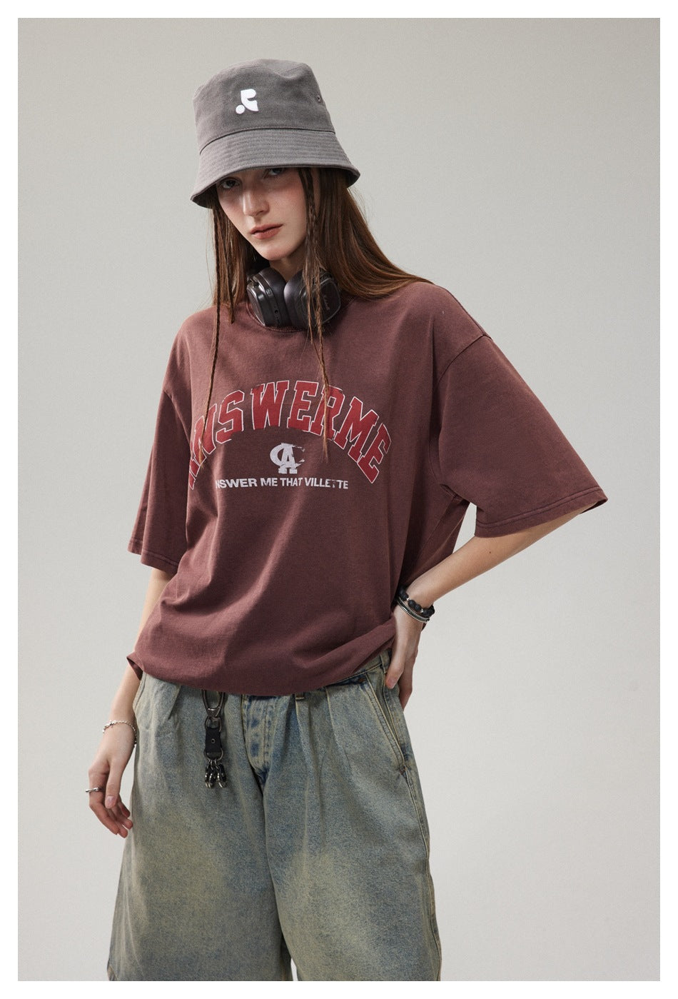 Model wearing an oversized burgundy graphic T-shirt, gray bucket hat, and loose faded gray jeans.
