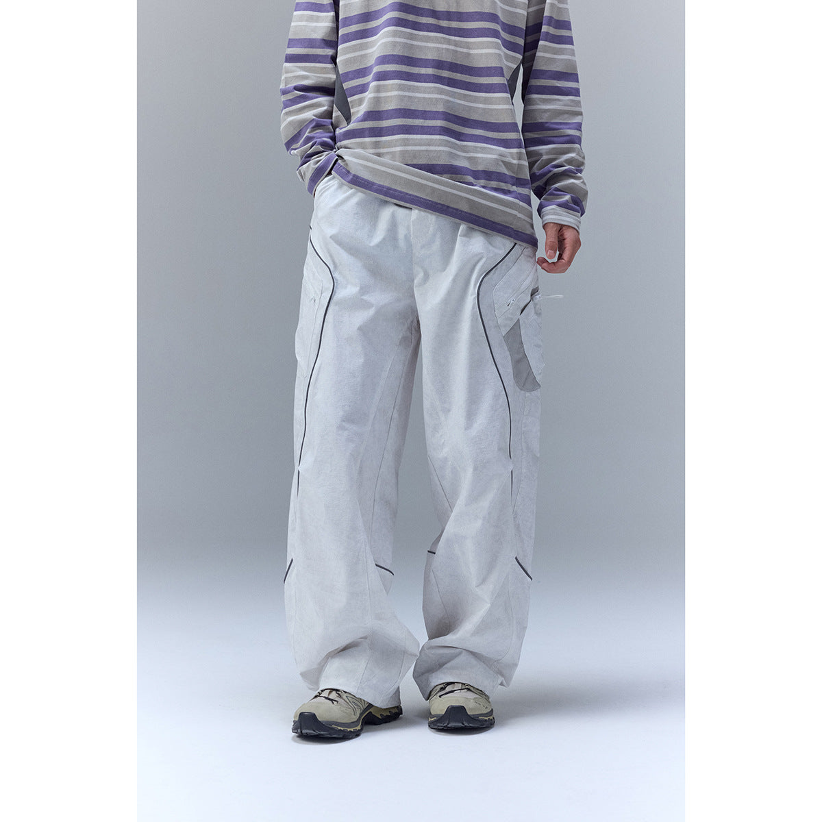 Cropped model wearing pale gray wide-leg cargo trousers with dark piping and a gray-purple striped shirt.