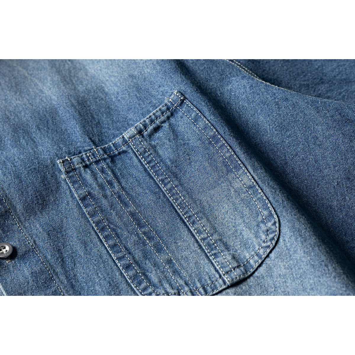Close-up of a blue denim shirt pocket with visible double-row stitching.