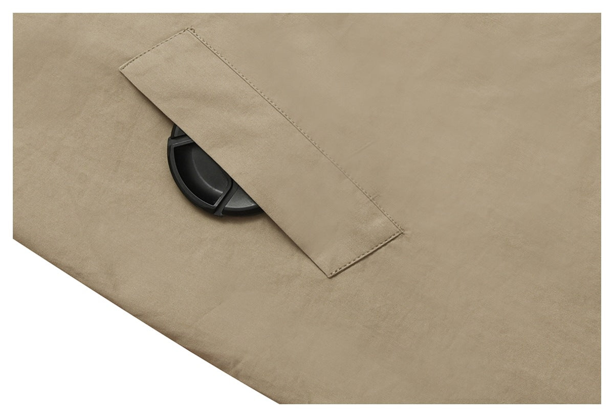 Close-up of a beige garment with a stitched fabric tab covering part of a black circular fastener.