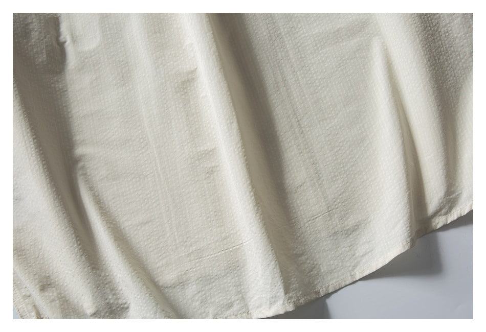 Close-up of the ivory shirt's textured fabric and curved lower hem.