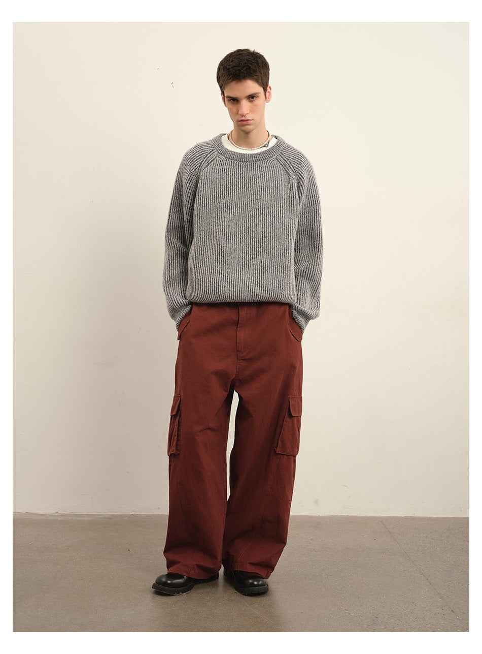 Full-length front view of a male model wearing a gray ribbed sweater, rust-red cargo pants, and black shoes.