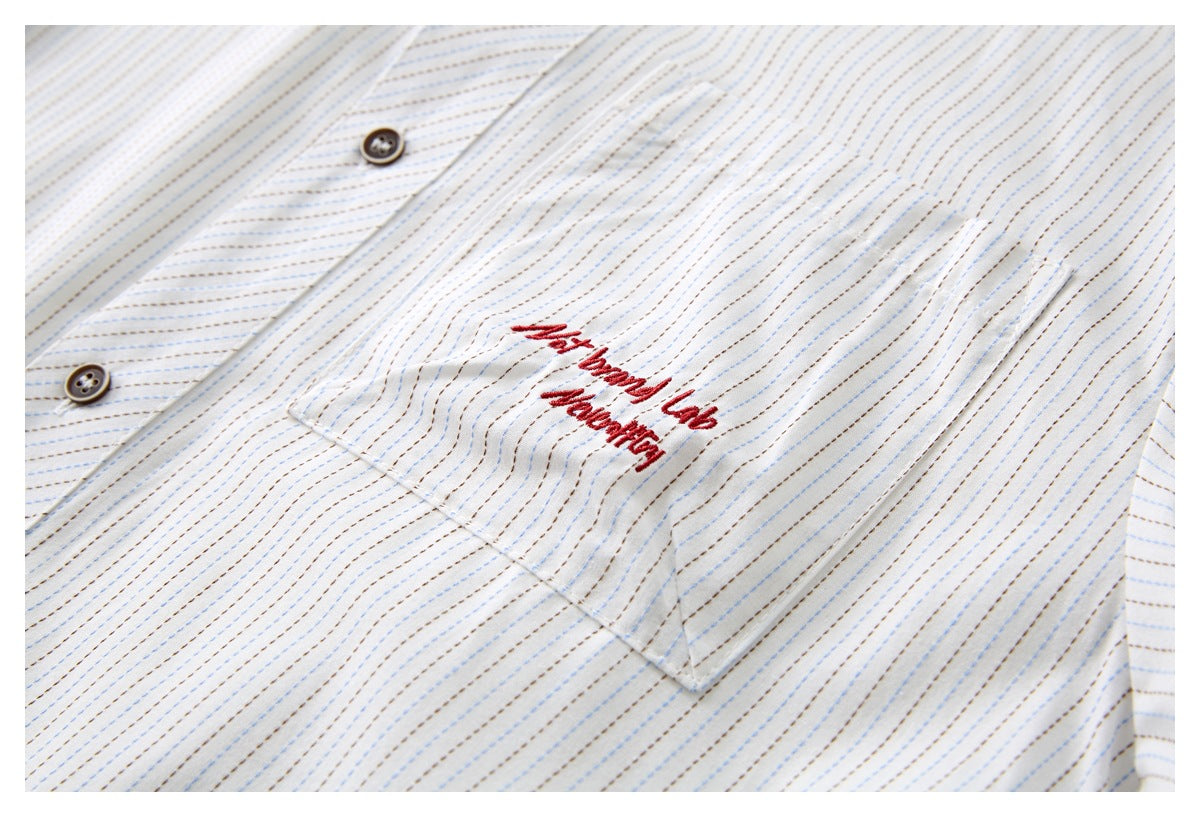 Close-up of a striped white shirt pocket with red cursive embroidery beside the button placket.