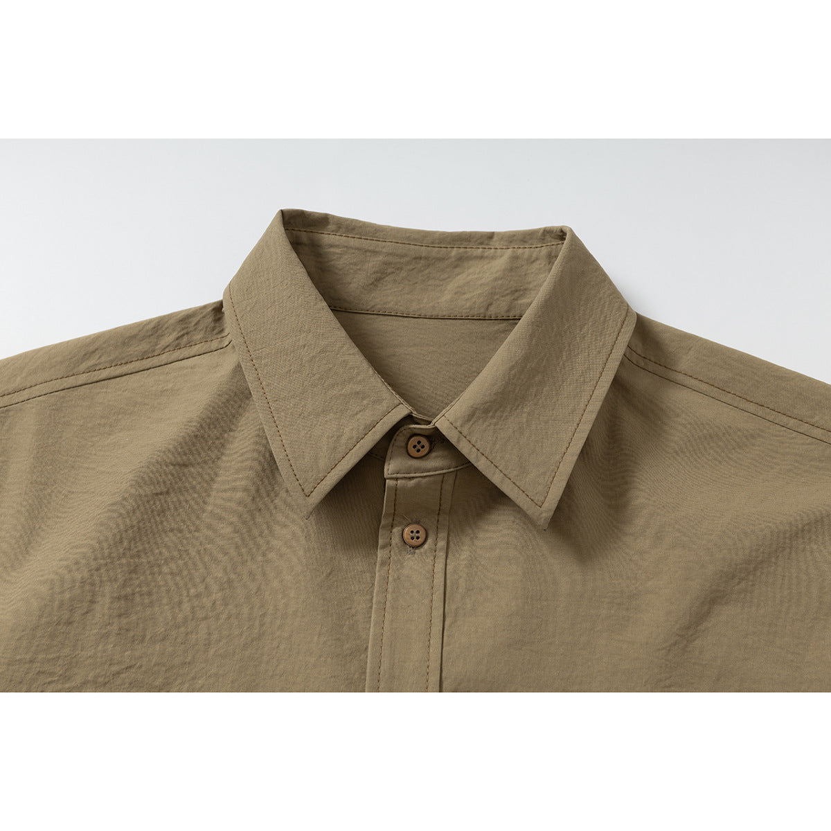 Close-up of a tan short-sleeve shirt's pointed collar, shoulder seams, and brown front buttons.