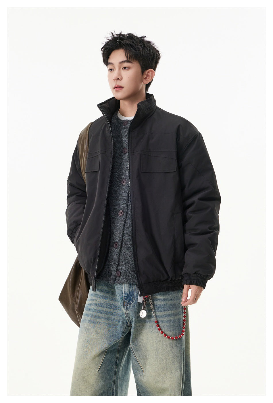 Model wearing a black stand-collar zip jacket open over a gray knit cardigan, three-quarter view with jeans