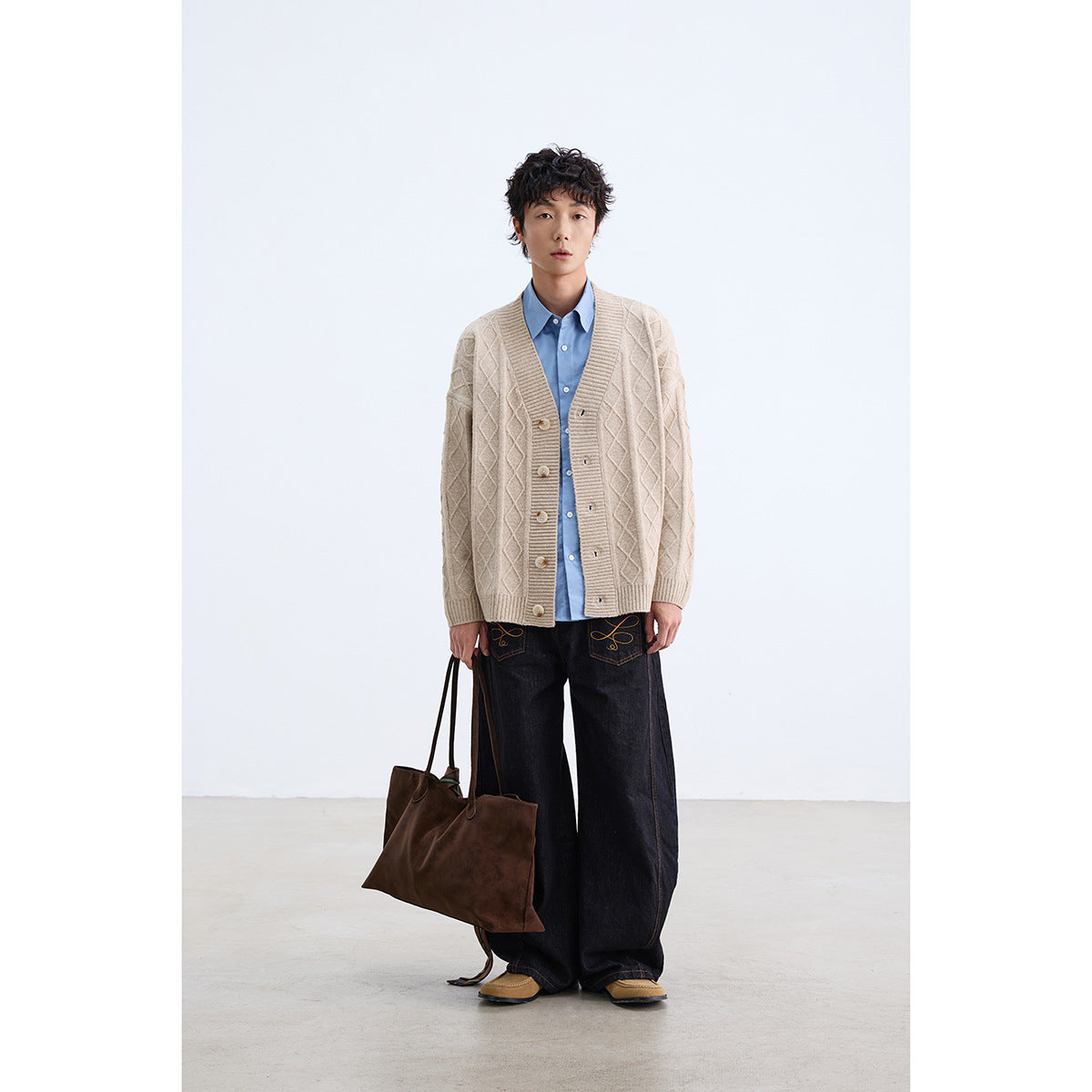 Model wearing a cream diamond-knit button-front cardigan over a blue shirt, with dark wide-leg jeans.