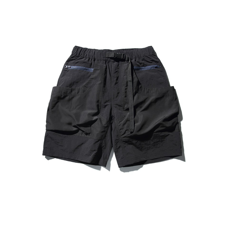 Black utility shorts with elastic waist, webbing belt, navy zippered pockets and large side patch pockets, flat lay