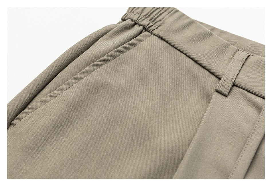 Close-up of taupe trousers showing the waistband, belt loop, and stitched pocket edge.