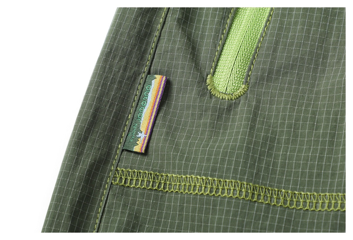 Close-up of olive-green grid-patterned fabric with lime stitching, a woven label, and looped seam trim.