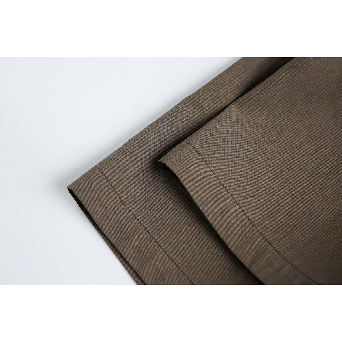 Close-up of the stitched hem and folded edge of a brown garment against a pale background.
