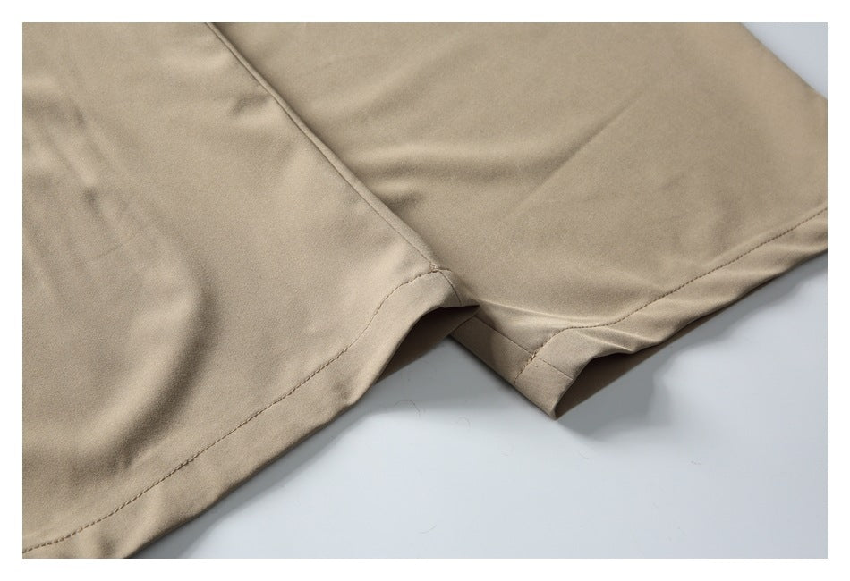 Close-up of the stitched hems and overlapping legs of beige trousers.