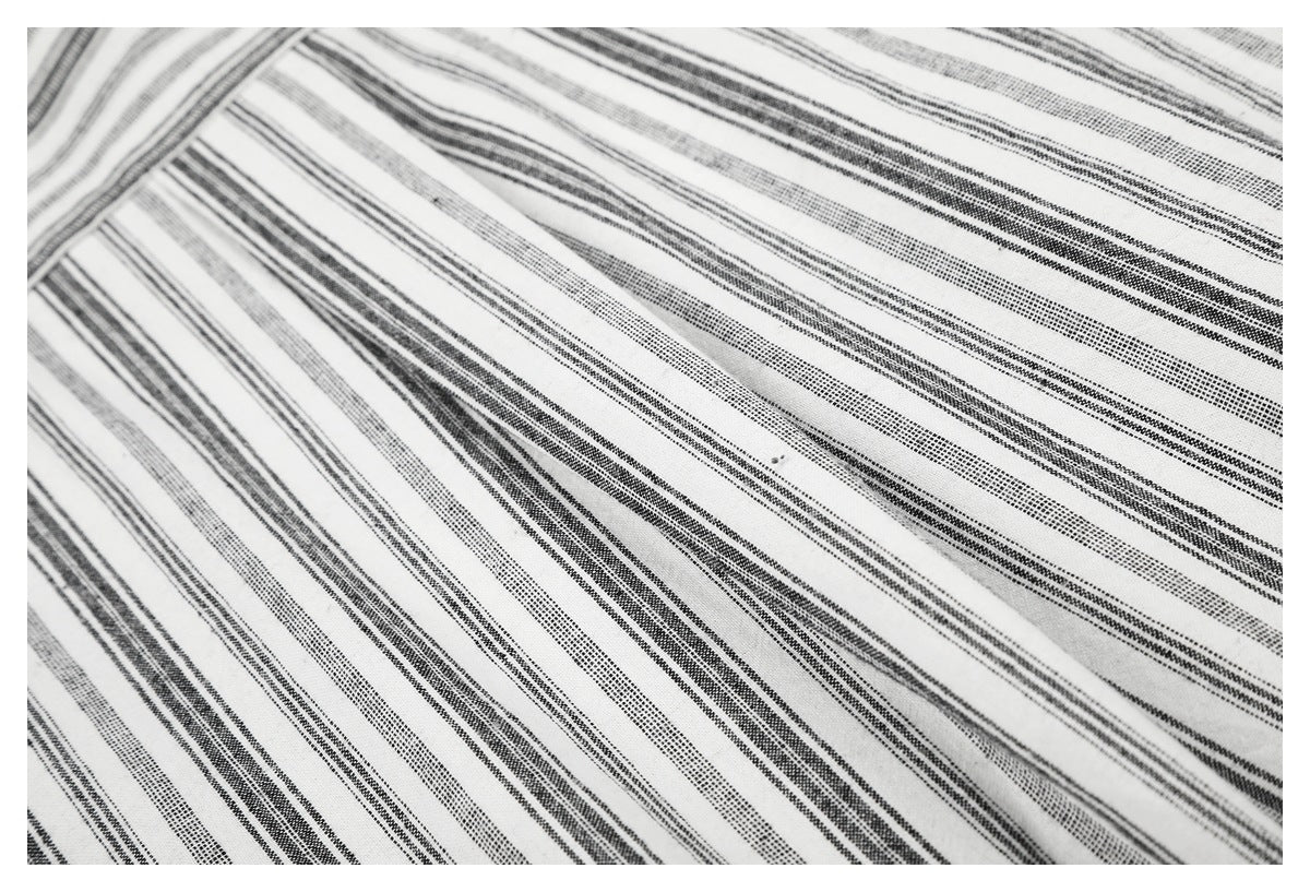 Close-up of white fabric with repeating black and gray stripe patterns laid flat.