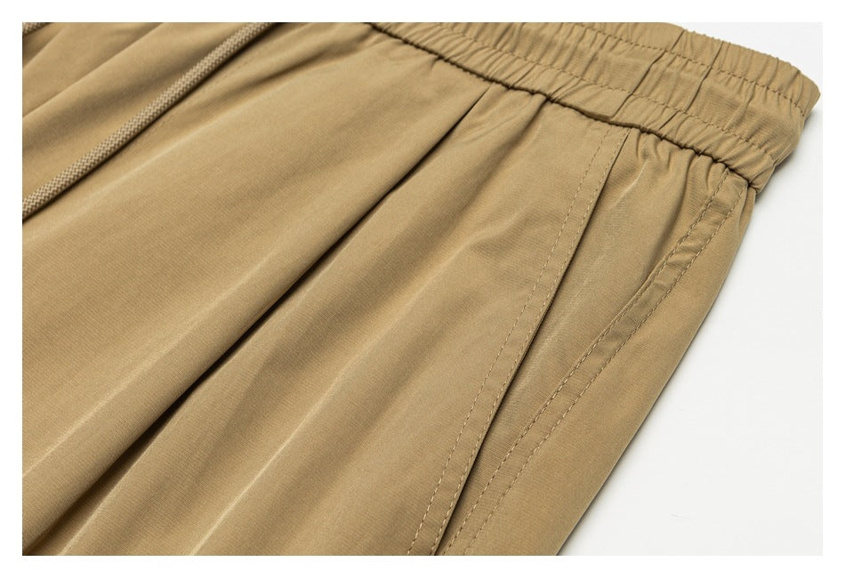 Close-up of tan pants showing the elastic waistband and stitched side pocket opening.