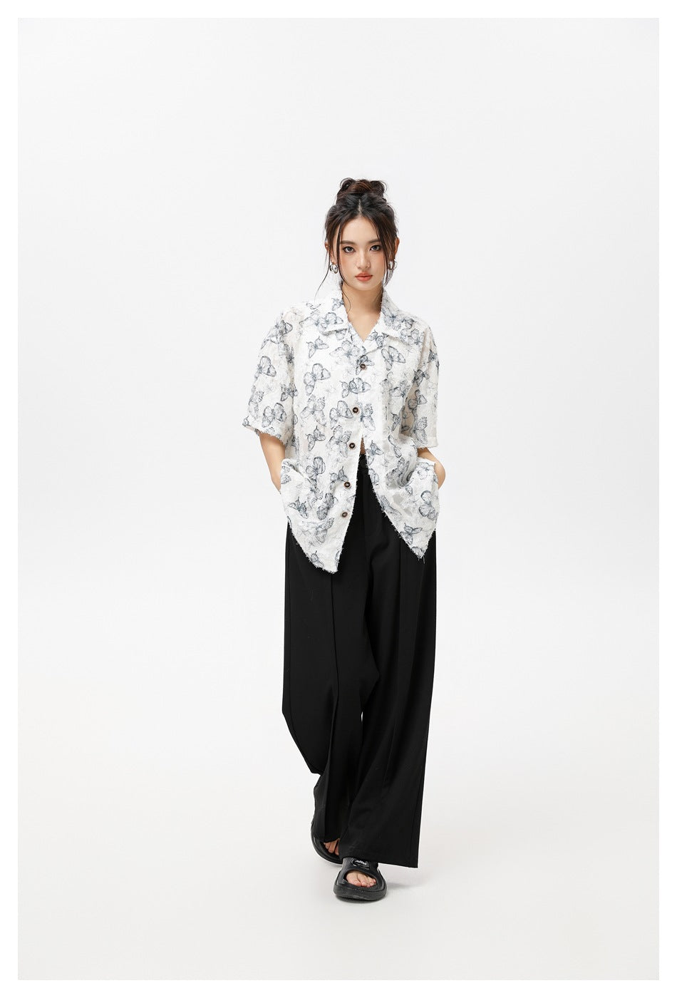 Front view of a model in an oversized white butterfly-print shirt with dark buttons and black wide-leg pants.