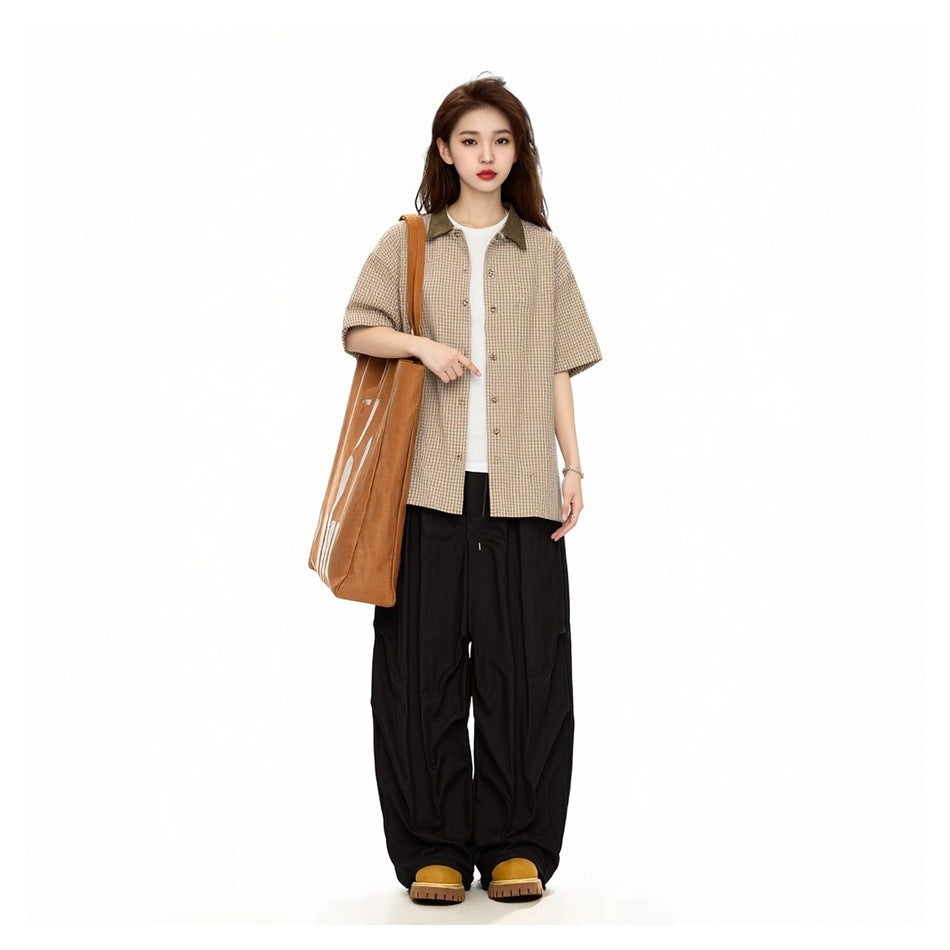 Model wearing the tan check short-sleeve shirt open over a white tee with black wide pants and a tote bag