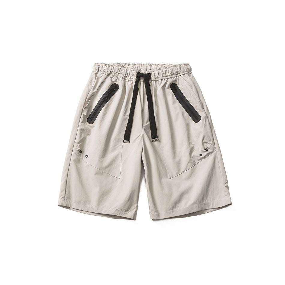 Beige-gray knee-length shorts flat lay with black drawstring, zippered diagonal pockets and front leg panels