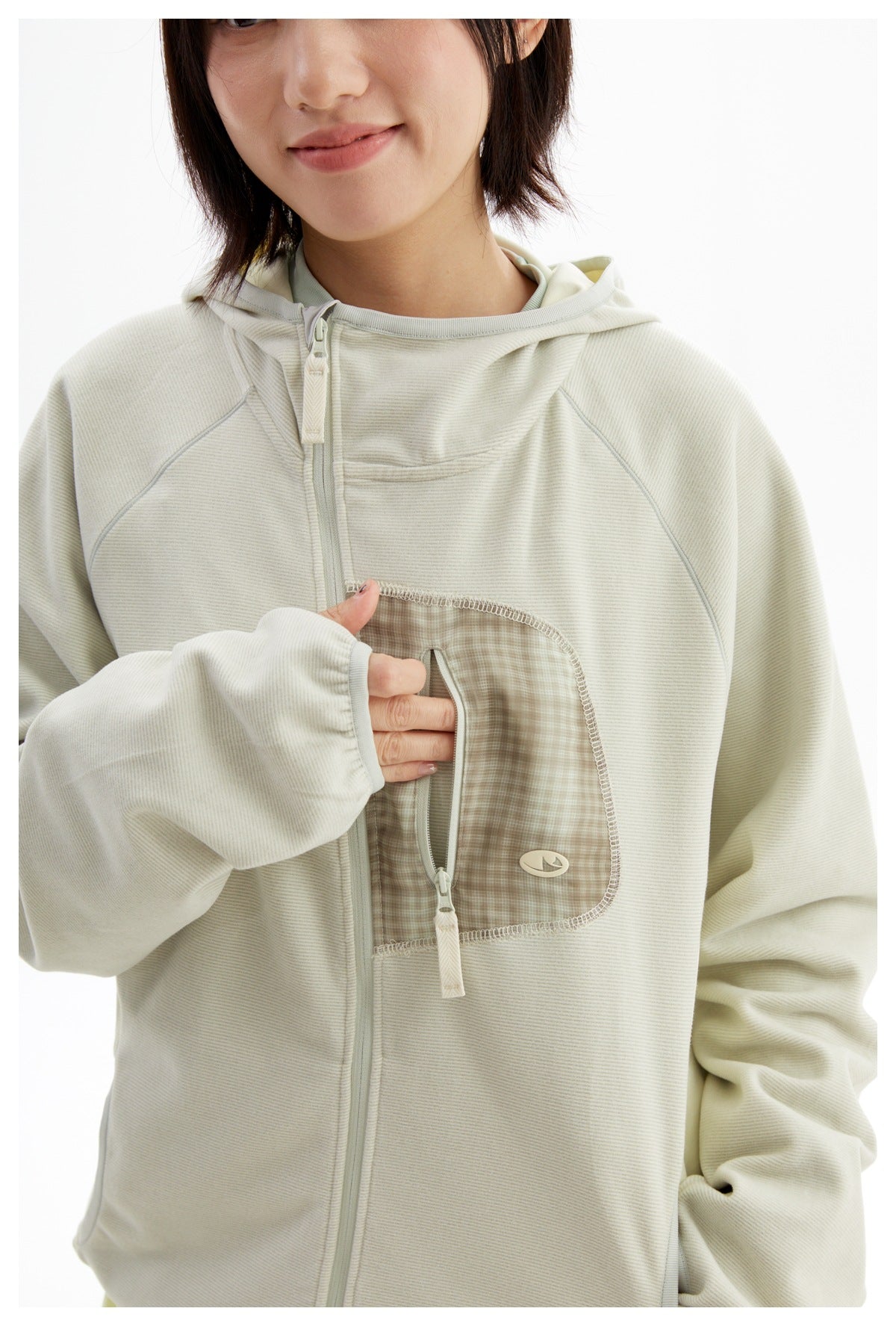 Close-up of a model wearing an ivory hooded zip jacket, showing its checked zip chest pocket and raglan seams.
