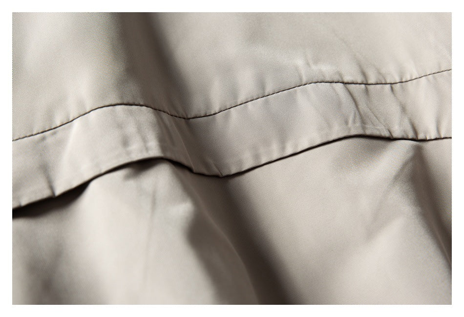 Close-up of a curved stitched seam and overlapping panel on light taupe jacket fabric.